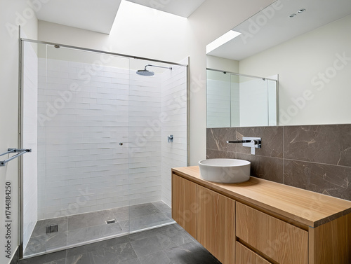 Minimalist bathroom with walk-in shower, floating oak vanity, and stone tile finishes illuminated by natural skylight
