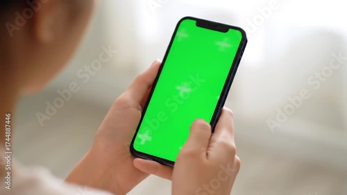 Over the shoulder view of a person using a smartphone with a green screen.