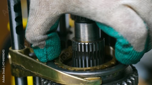 Car mechanic in gloves assembling automotive manual gearbox transmission, installing metal gears on main shaft during detailed repair service in workshop. Mechanic assembling car transmission gearbox
