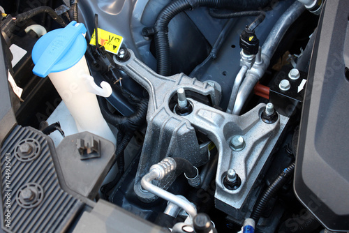 Close-up of vehicles top engine mount showing metal components, bolts, and wiring under hood of electric vehicle. Engine mount new car. Engine parts under the hood of the car.