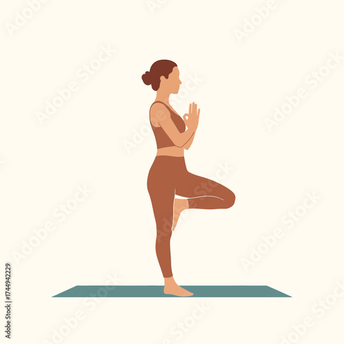 Woman in brown sportswear performing tree pose yoga on a mat, hands in prayer position.