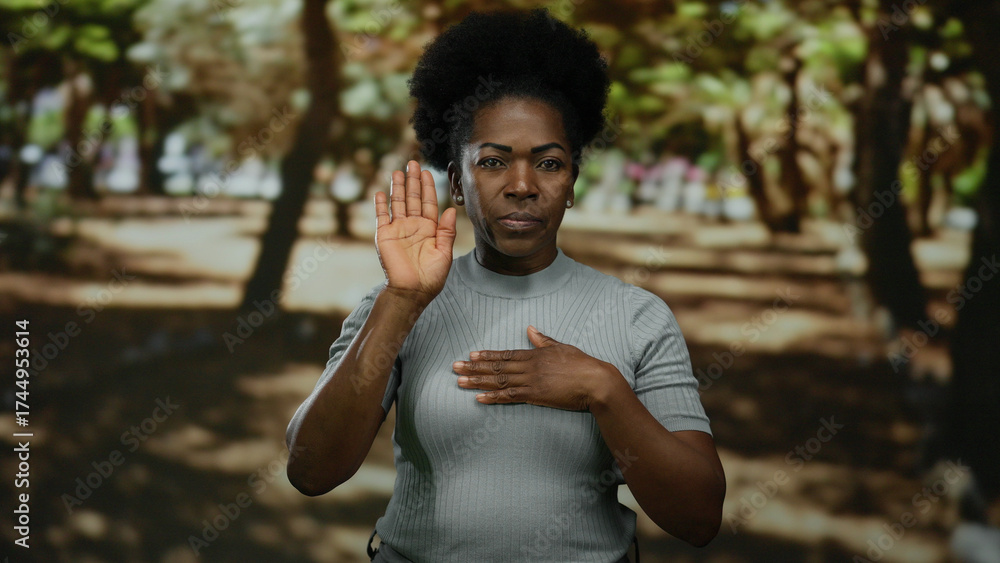 Fototapeta premium Woman gesturing oath in park with trees, demonstrating a serious expression, wearing casual attire outdoors.