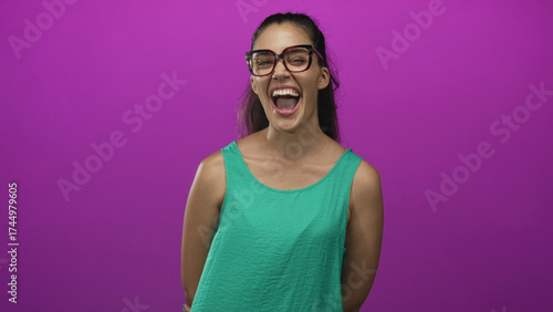 Photography Woman in glasses and green top with expressive grin winks and smiles towards camera in purple studio; playfulness