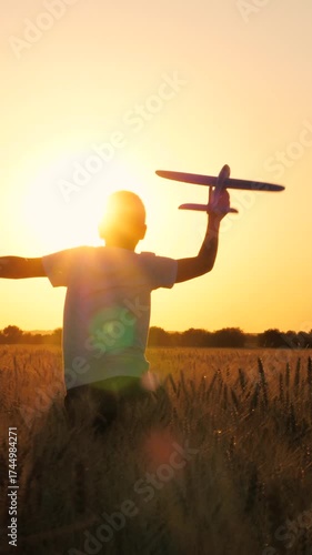 Happy male teenager running with aircraft toy flying pilot imagination at sunset sunrise wheat field back view. Joyful boy kid child silhouette playing plane plaything fantasy flight game meadow dusk
