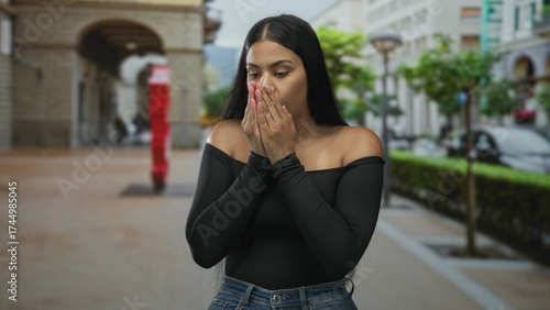 Photos Latin woman hugging arms on street pavement lined with arches and lampposts in daylight; vulnerability