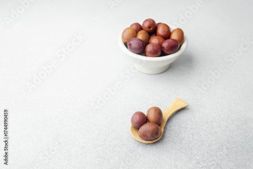 Kalamata olives in white bowl and wooden spoon on bright background
