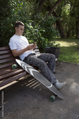 Adult skateboarder sitting in city park on bench an looking at smart phone screen