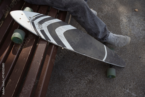 Close up: skateboard and leg of rider sitting in city park on bench