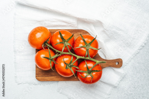 Fresh tomatoes on a wooden cutting board with a white cloth backdrop