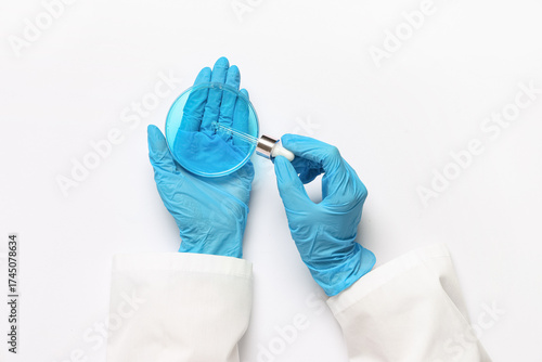 Scientist taking sample from Petri dish with blue liquid on white background