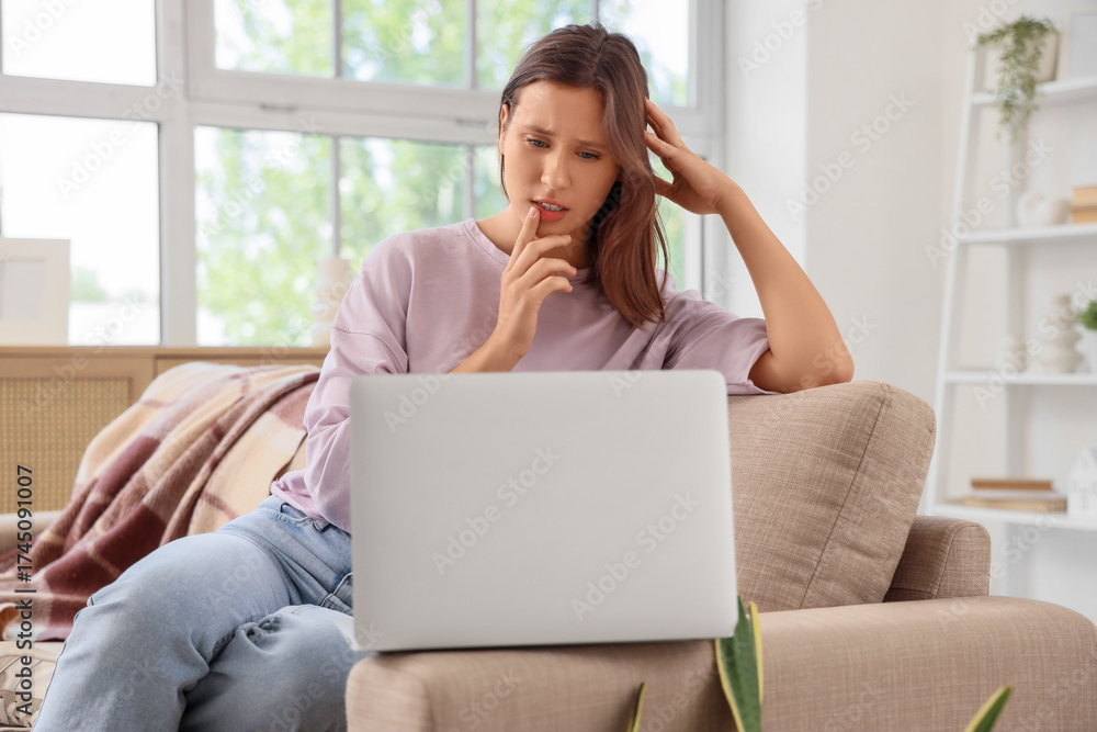 Naklejka premium Beautiful young thoughtful woman with laptop sitting on sofa in living room at home