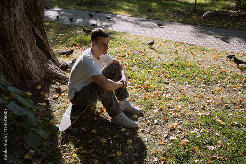 Adult man sitting on skateboarder in city park in summer day