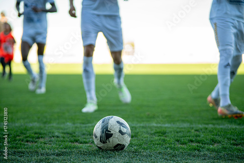 Close-up of a football on green grass with blurred players in the background, symbolizing teamwork, competition, and the spirit of the game.