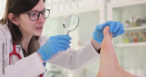 Female doctor examines patient foot with magnifying glass at medical consultation in hospital. Medic checks skin condition diagnosing disease