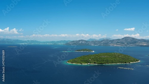 A green island archipelago and an oyster farm in the foreground of a Croatian seascape. A long mountain range is visible on the distant horizon under a beautiful blue sky. Panoramic view.