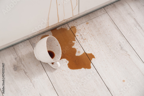 Fotografie Overturned cup and spilled coffee on floor in kitchen