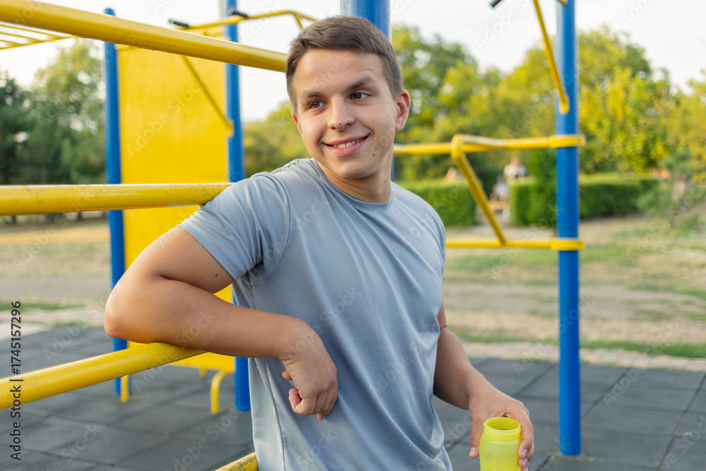 Fototapeta premium A young man standing on an outdoor sports ground drinking water after a workout