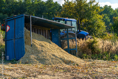 Overturned blue farm trailer with spilled corn beside tractor after accident on agricultural field during harvest