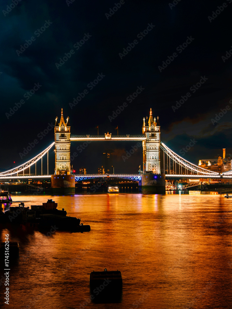 Fototapeta premium London city night skyline and Tower Bridge with golden glow and water reflections in the River Thames, United Kingdom.