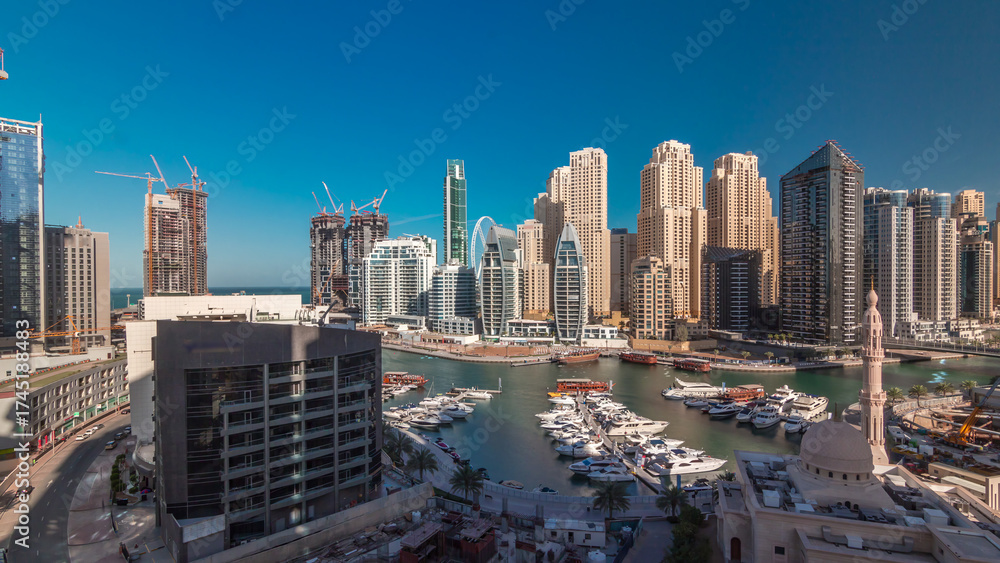Naklejka premium Yachts in Dubai Marina flanked by the Al Rahim Mosque and residential towers and skyscrapers aerial timelapse.
