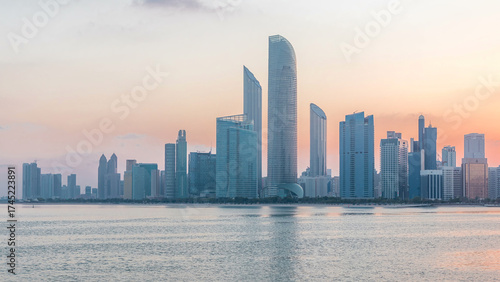 Abu Dhabi city skyline with skyscrapers before sunrise with water reflection night to day timelapse