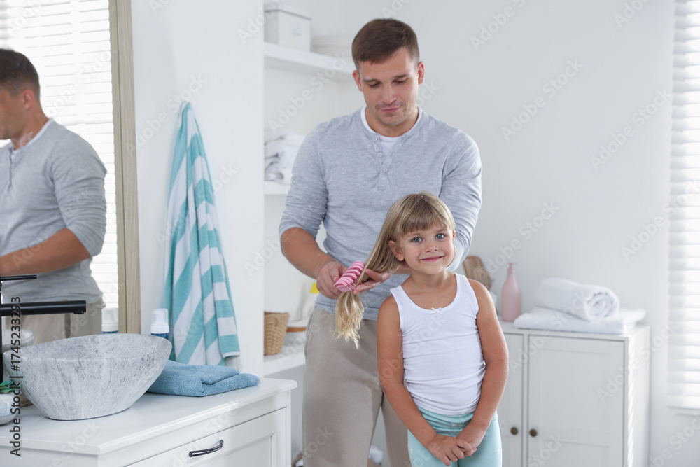 Fototapeta premium Father brushing his daughter's hair in bathroom