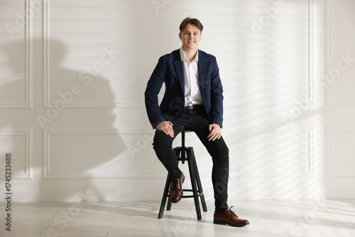 Bild auf Leinwand Man in stylish jeans on stool near white wall indoors