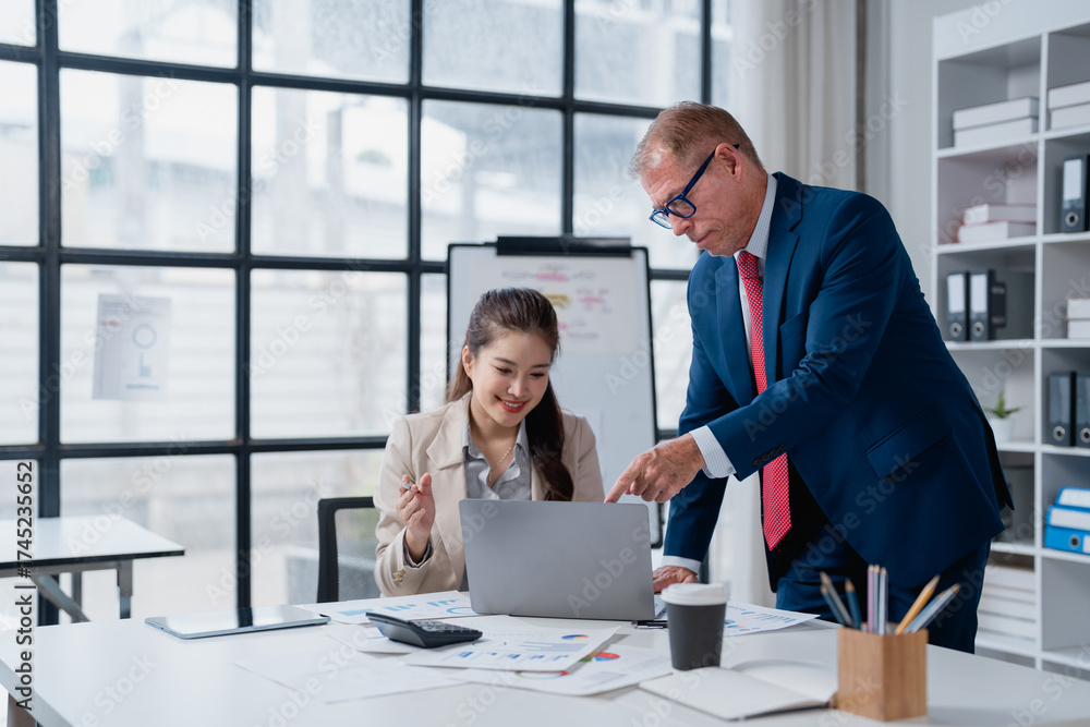 Fototapeta premium Business executive mentoring young female employee, pointing at laptop screen while discussing charts and working together on a project in a modern office workplace