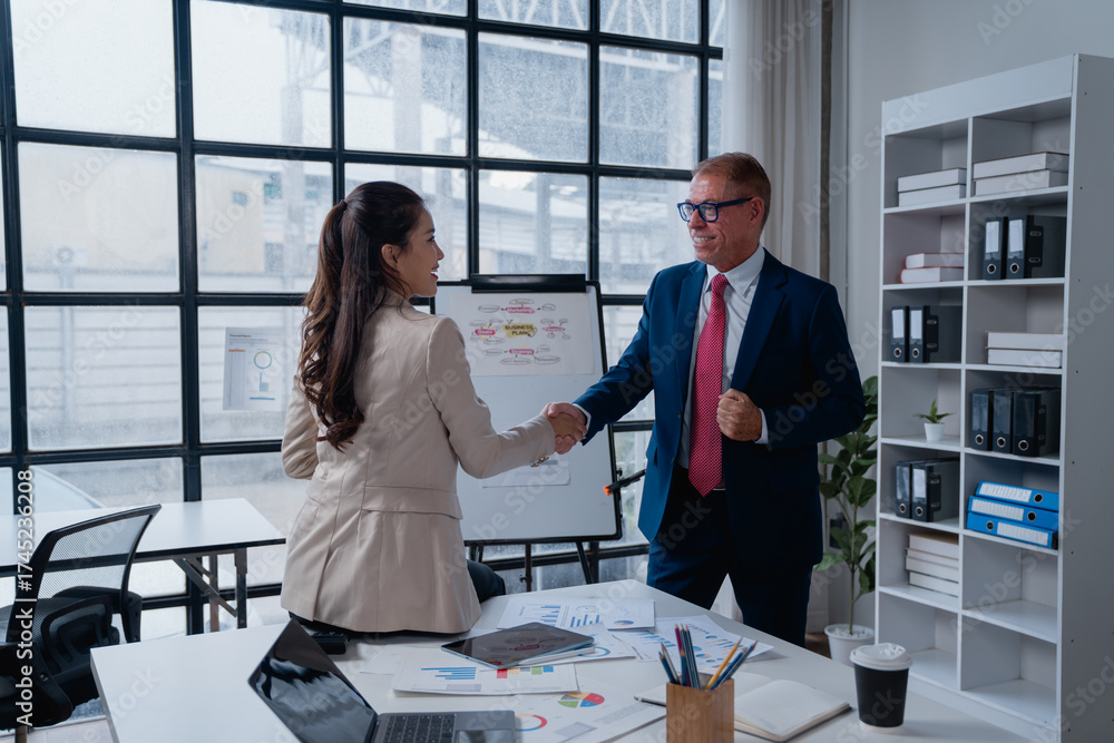 Fototapeta premium Businesswoman and businessman smiling, exchanging a handshake in an office setting, celebrating successful collaboration and reaching a new career milestones