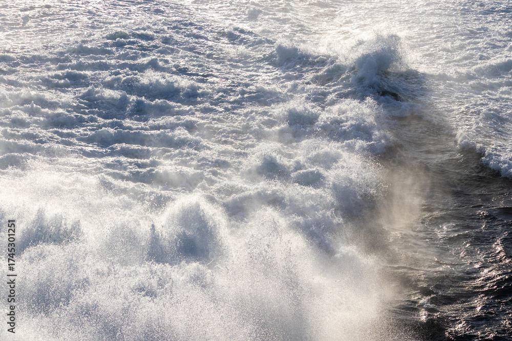 Obraz premium Dynamic ocean waves generating abundant white foam and fine mist under bright natural light.