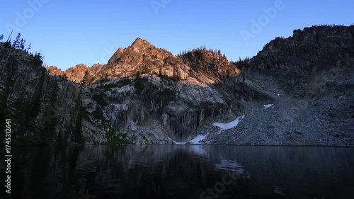 Sunlight illuminates the rugged peaks above Lower Trail Creek Lake in Idaho’s Sawtooth National Forest at sunset, above calm alpine waters.