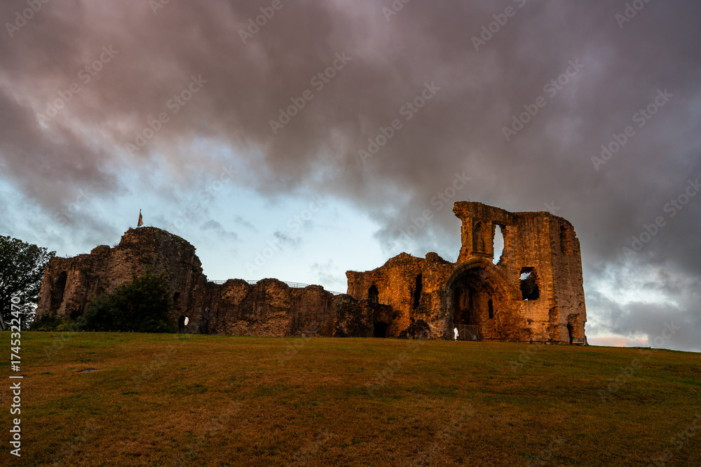 Obraz premium Warm early sunlight illuminating the ancient stone ruins of Denbigh Castle under dramatic morning clouds