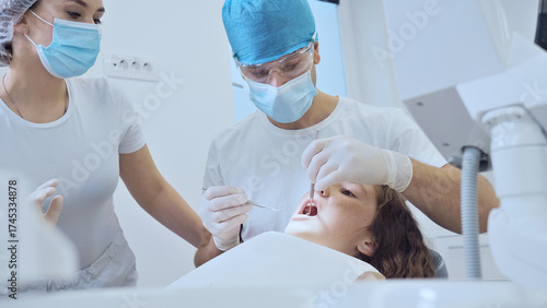 A diverse dental team in blue attire examines a young patient in a modern clinic, emphasizing dental health and professional care.
