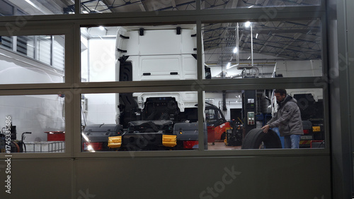 An establishing shot in an auto repair shop, a mechanic works on a vehicle chassis. The industrial setting features tools and equipment.