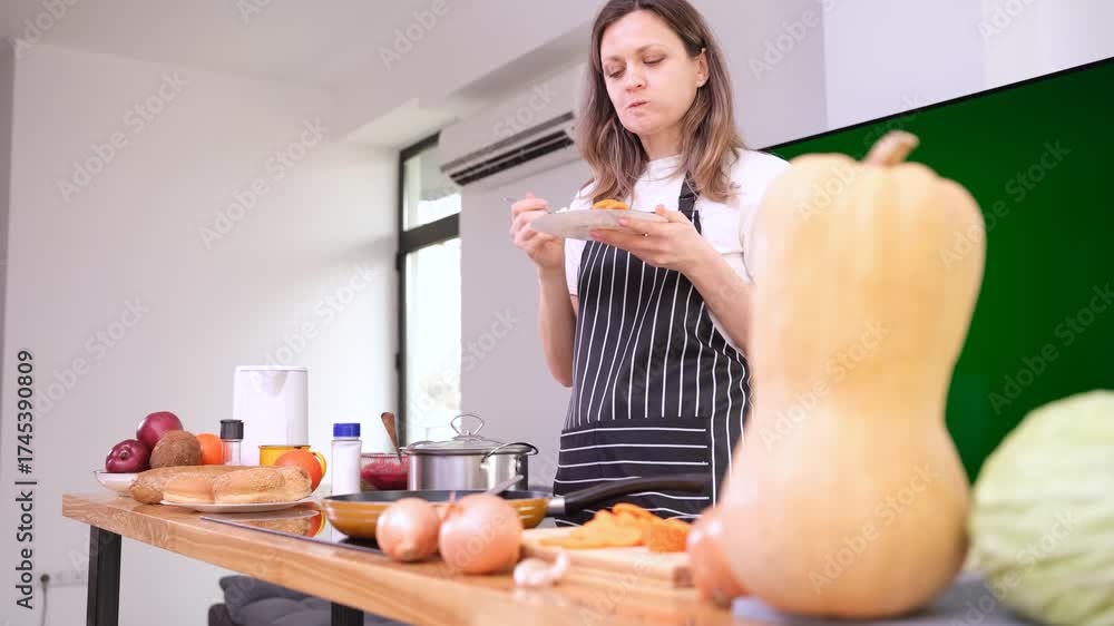 Young woman chef in apron enjoys slice of freshly baked pumpkin pie with delighted smile. Housewife enjoys taste of homemade pumpkin pie in kitchen