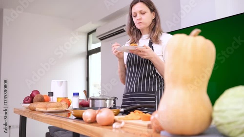 Young woman chef in apron enjoys slice of freshly baked pumpkin pie with delighted smile. Housewife enjoys taste of homemade pumpkin pie in kitchen