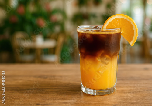 Bumble coffee refreshing beverage in a glass filled with orange juice and ice and topped with a dark espresso layer on a wooden table of modern cafe.