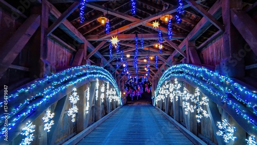 Visitors cross a beautiful wooden bridge adorned with vibrant blue lights and snowflake decorations. The festive atmosphere creates a magical experience for all who walk through.