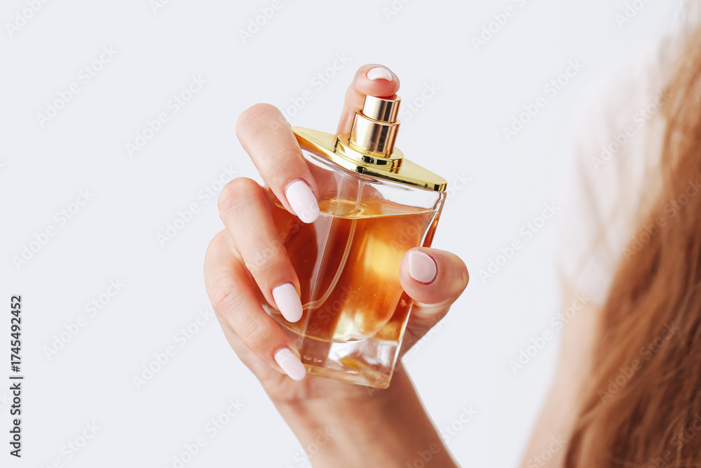 Naklejka premium Woman holding perfume bottle with golden cap. Elegant glass fragrance container in female hand. Luxury aroma product on white background. Beauty and fashion detail for personal care concept.