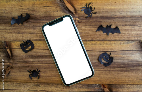 Mockup, smartphone, paper black bat, spiders and pumpkins on wooden background. Halloween background.