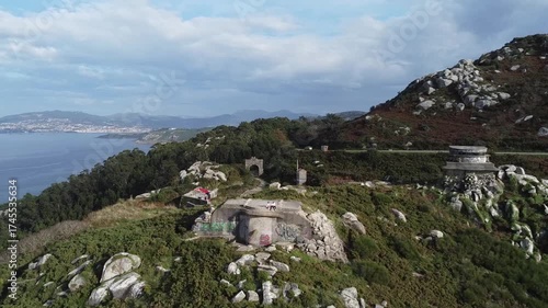 Aerial drone footage moving away from Cabo Silleiro's military ruins, capturing rocky terrain, lush greenery, and sweeping views of the Atlantic Ocean and surrounding landscapes in Galicia, Spain  
