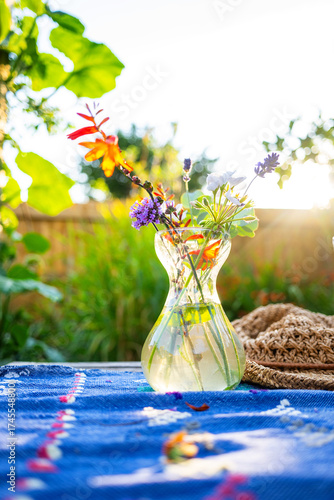 Obraz na plátně Garden flowers in a small glass vase outside on a sunny patio table