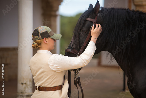 Portrait of young horsewoman caressing her black Spanish thoroughbred horse, with affection and tenderness showing her love. Concept horse riding, horsewoman, horse, dressage.