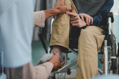 The hands of doctor or physical therapist's examine a young man with disability in a wheelchair for muscle stiffness and dyskinesia are common symptoms in people with CP or cerebral palsy.