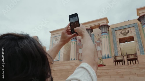 A tourist takes a photo of a colorful building with columns in Ouarzazate, Morocco. The focus is on the moment of capturing the image with a smartphone,