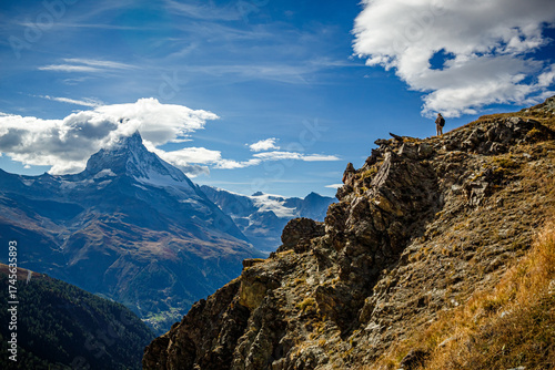 A lone tourist looks down from a high cliff at the summit of the Matterhorn.