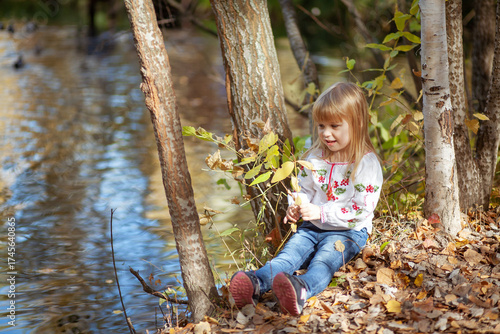 Child Enjoying Autumn by the Water While Gathering Colorful Leaves on a Sunny October Day in the Park