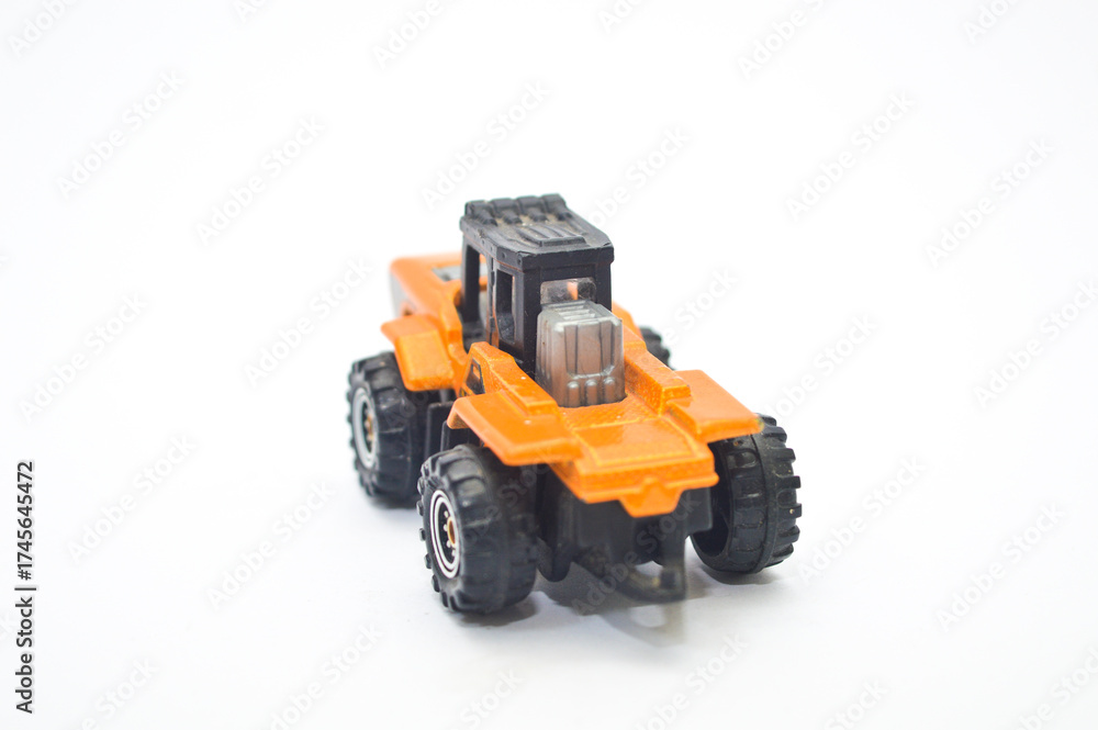 Fototapeta premium Close-up of a well-worn orange and black die-cast toy tractor, construction vehicle, isolated on a white background. Represents childhood, engineering, industry, play, and transportation concept.