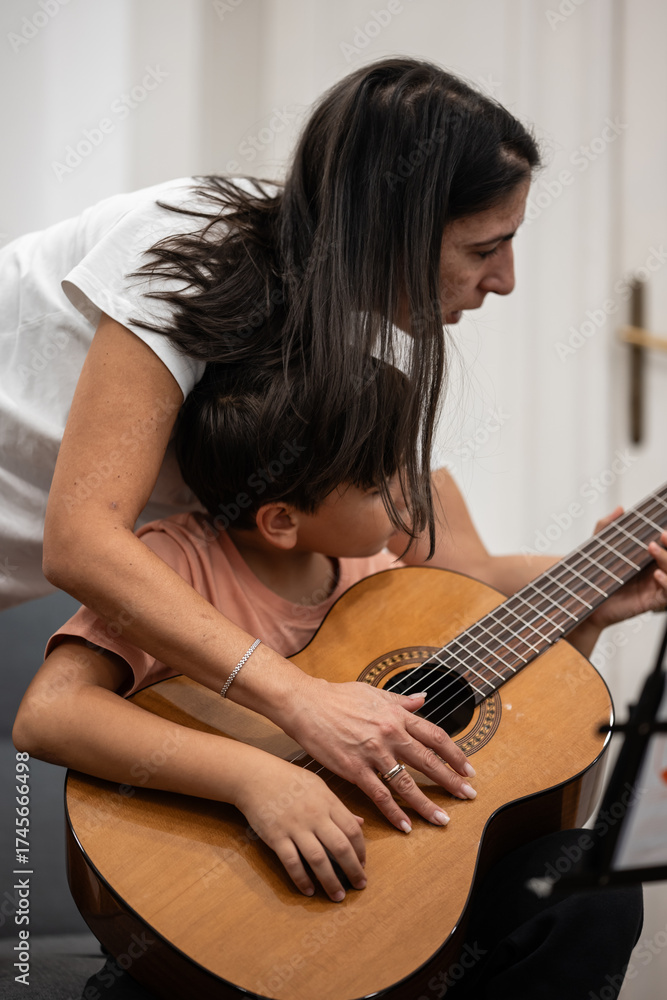 Fototapeta premium Mother teaching son playing acoustic guitar