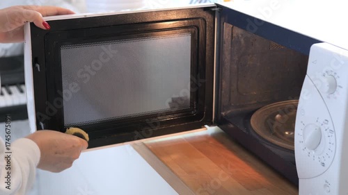 Woman is opening a microwave oven. The microwave is black and white. The microwave door is open